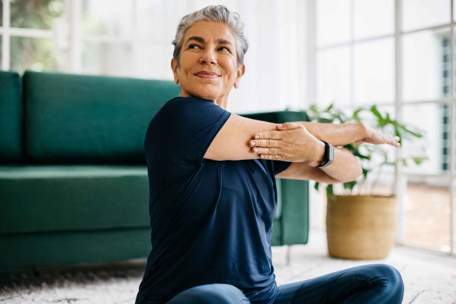 mature_woman_stretching_arm_at_home_health_joints_vitruvy