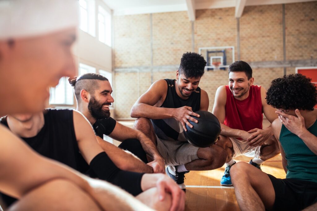 Shot of happy ethnic basketball players enjoying spending time together after practice while sitting on the court.