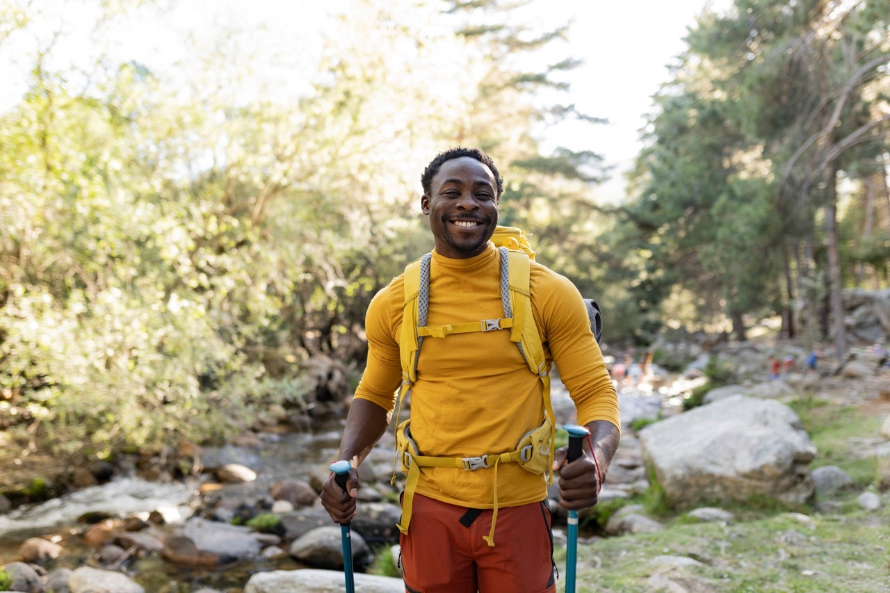 Cheerful middle age African American man trekking outdoors in the forest on a sunny day - Adventure lifestyle for people who love freedom and independence - Beautiful nature concept