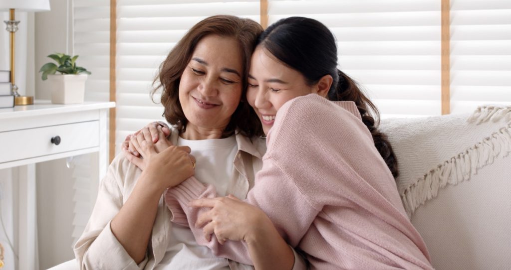 a woman sitting on the couch hugging another woman