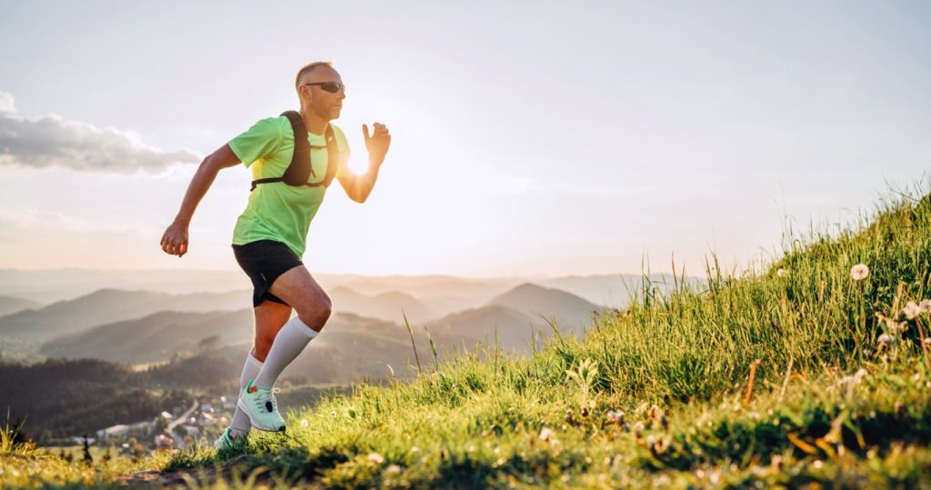 man with sunglasses running up a hill with sunset and mountains in background