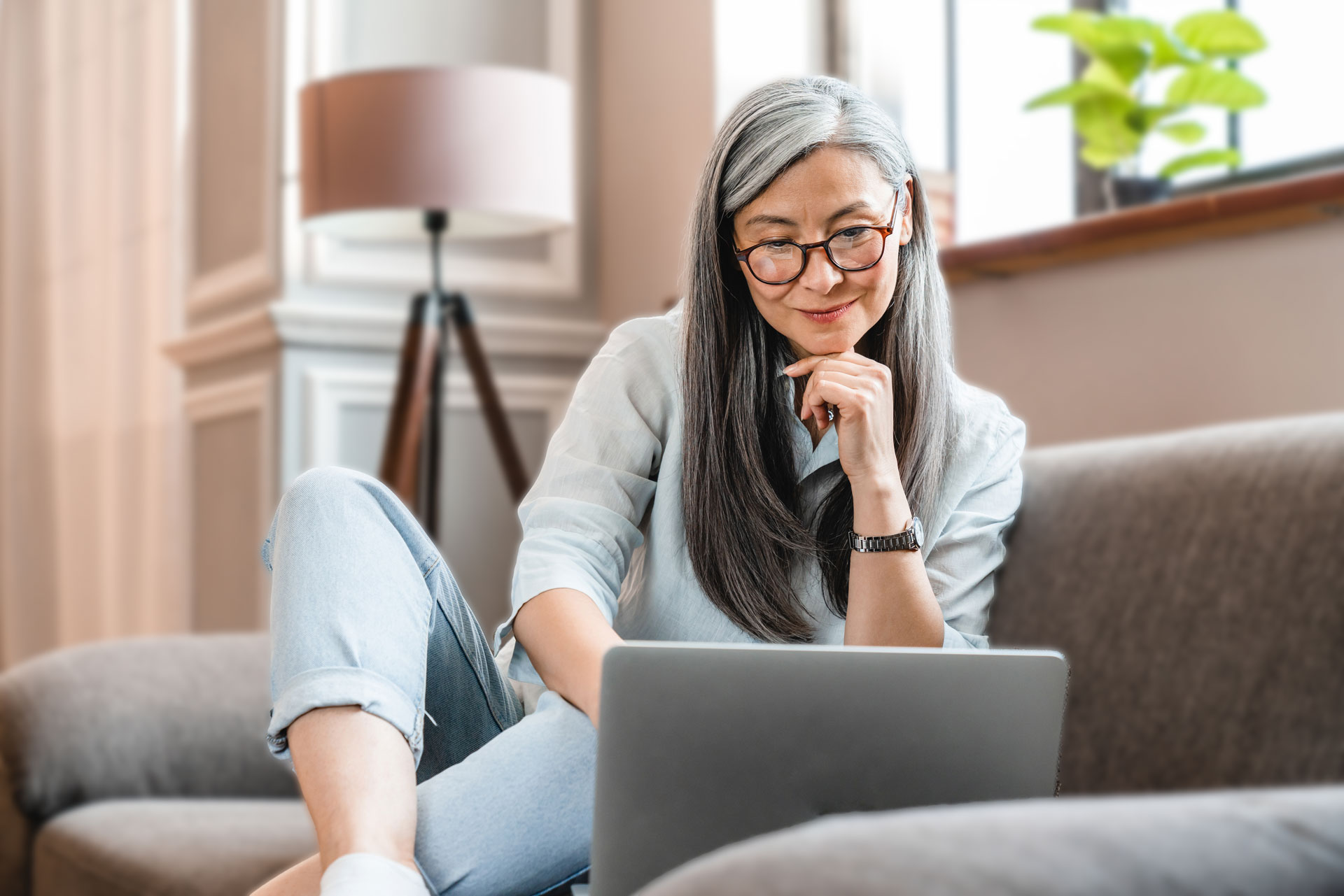 older woman with glasses on the couch with her laptop