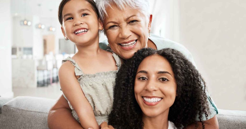 older woman smiling with a younger one next to her and a child in her arms