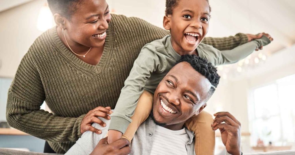 a family of 3 smiling while sitting on the couch